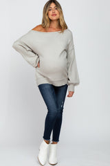 woman wearing a light gray maternity off-shoulder sweater and blue skinny jeans, displaying her baby bump