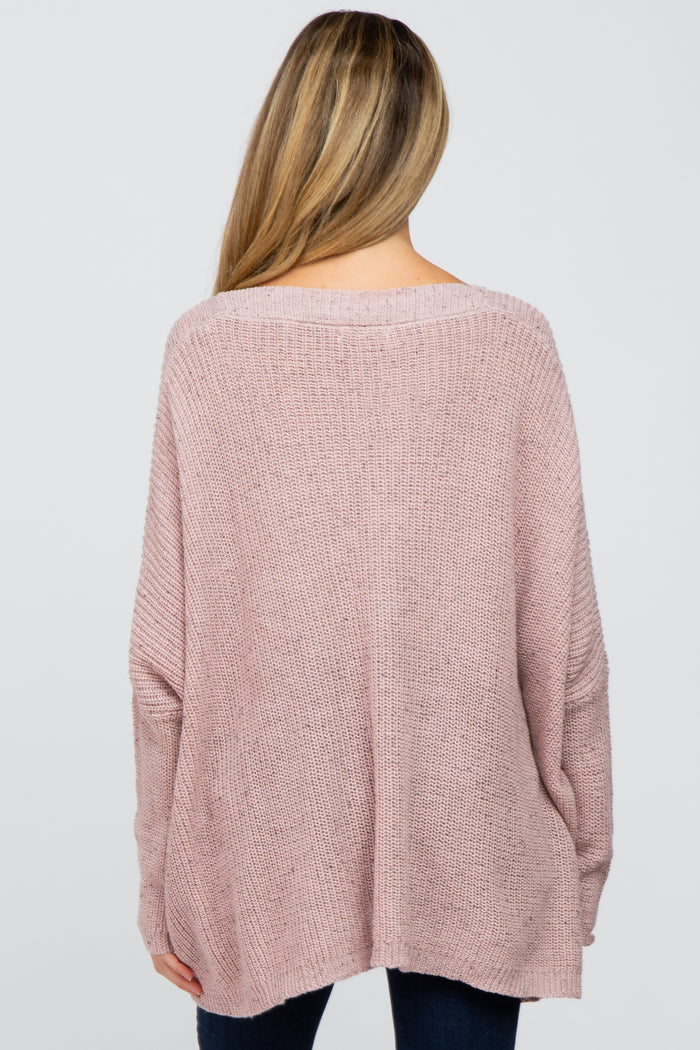 woman wearing a loose-fitting pale pink maternity sweater, seen from the back