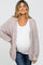 woman wearing a light pink oversized maternity cardigan over a white top and showing her baby bump