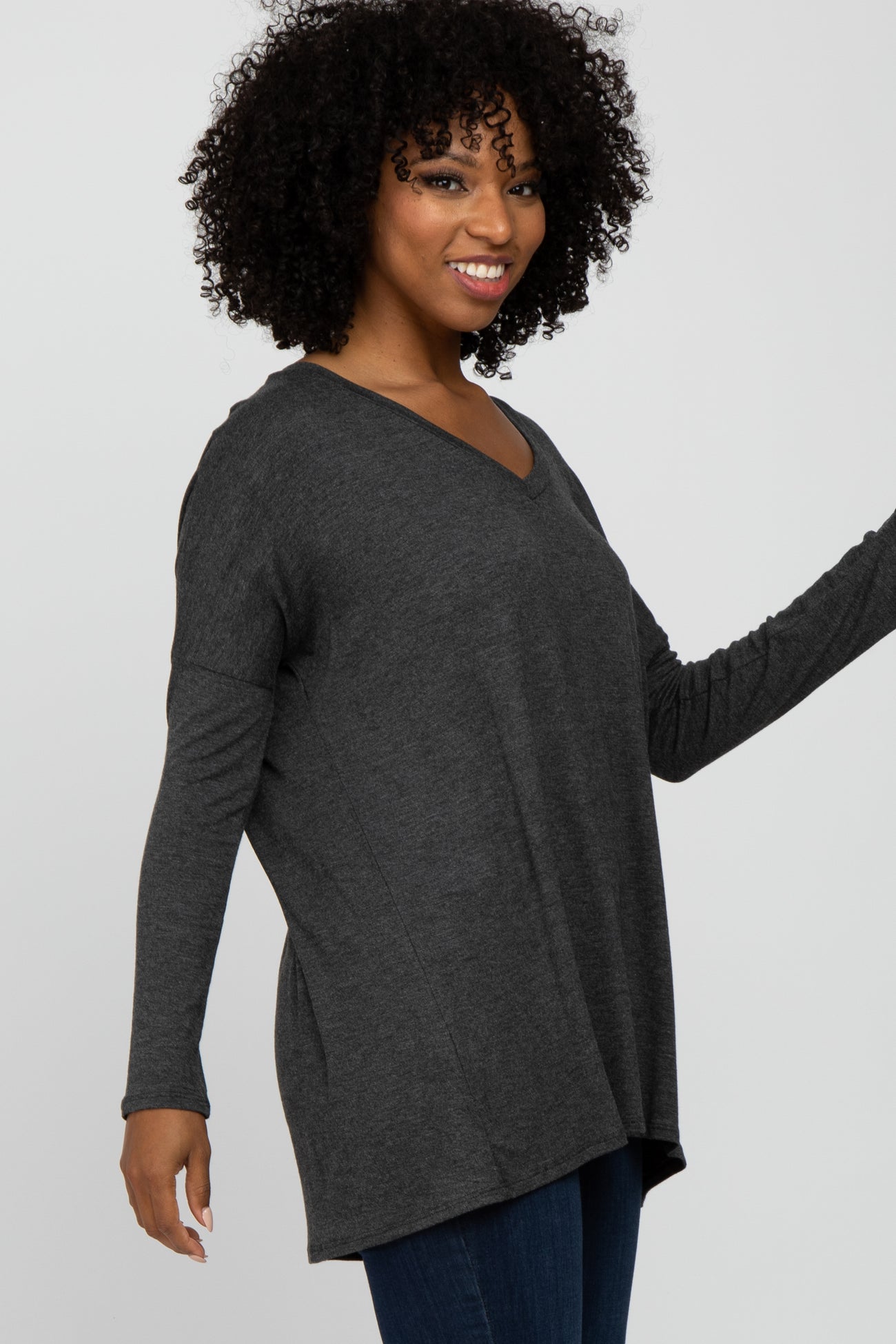 woman wearing a dark gray long sleeve v-neck top and smiling while posing with her hand raised