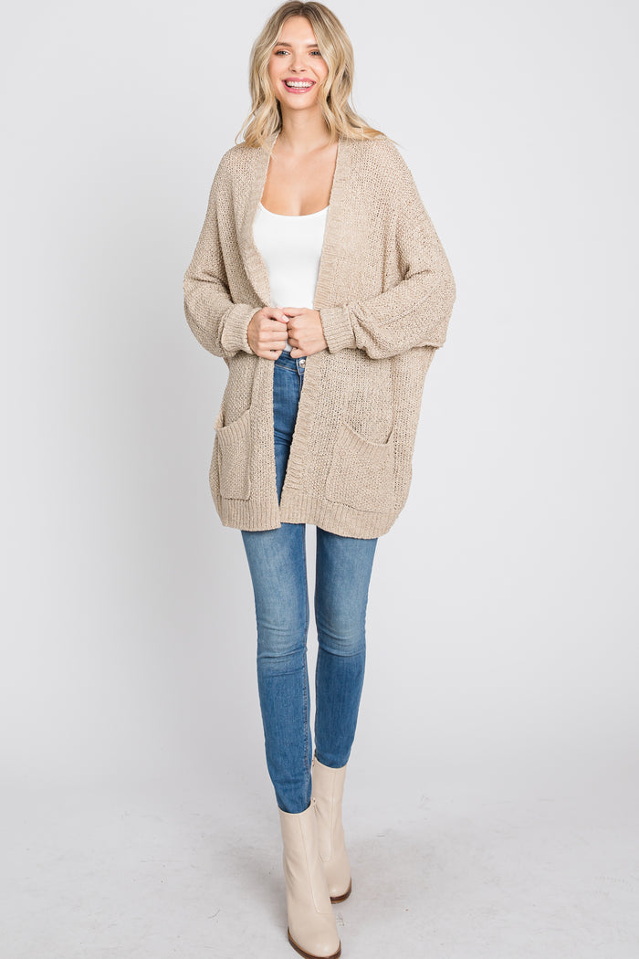 woman wearing a knitted beige cardigan with pockets, paired with a white tank top and blue skinny jeans