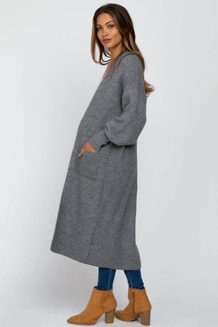 woman wearing a long gray maternity cardigan with pockets and a relaxed fit, paired with blue jeans and tan ankle boots