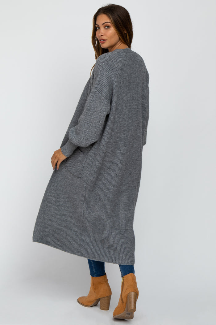 woman wearing a long gray maternity cardigan with loose sleeves, styled with fitted jeans and ankle boots