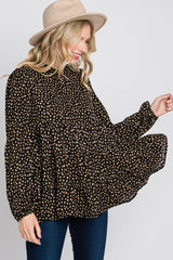 woman wearing a black and tan polka dot button-up shirt with a flowy silhouette and long sleeves, smiling while wearing a hat