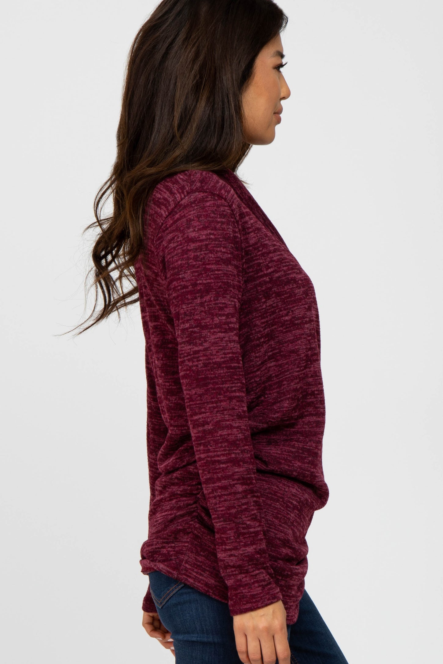 woman wearing a burgundy long sleeve sweater with a relaxed fit and side draping, styled with jeans