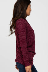 woman wearing a burgundy long sleeve sweater with a relaxed fit and side draping, styled with jeans