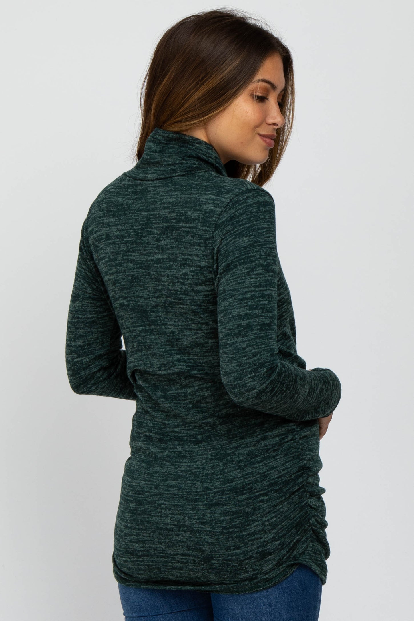 woman wearing a dark green maternity top with a high collar and ruching detail at the sides
