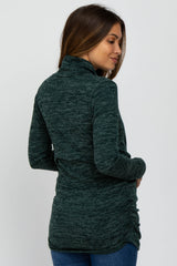 woman wearing a dark green maternity top with a high collar and ruching detail at the sides