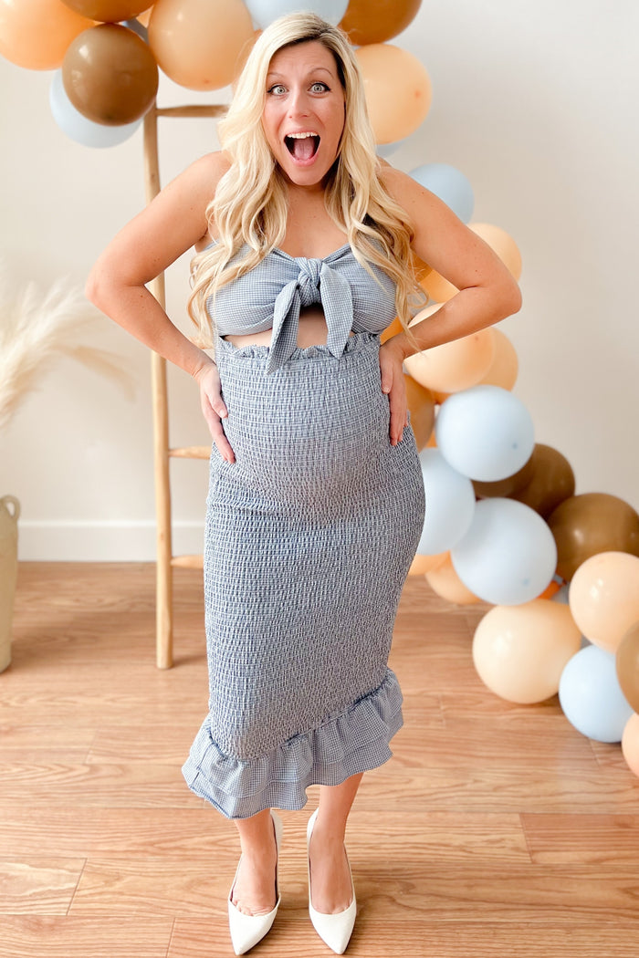 woman wearing a blue and white striped maternity dress with a tie front, showing her baby bump and smiling
