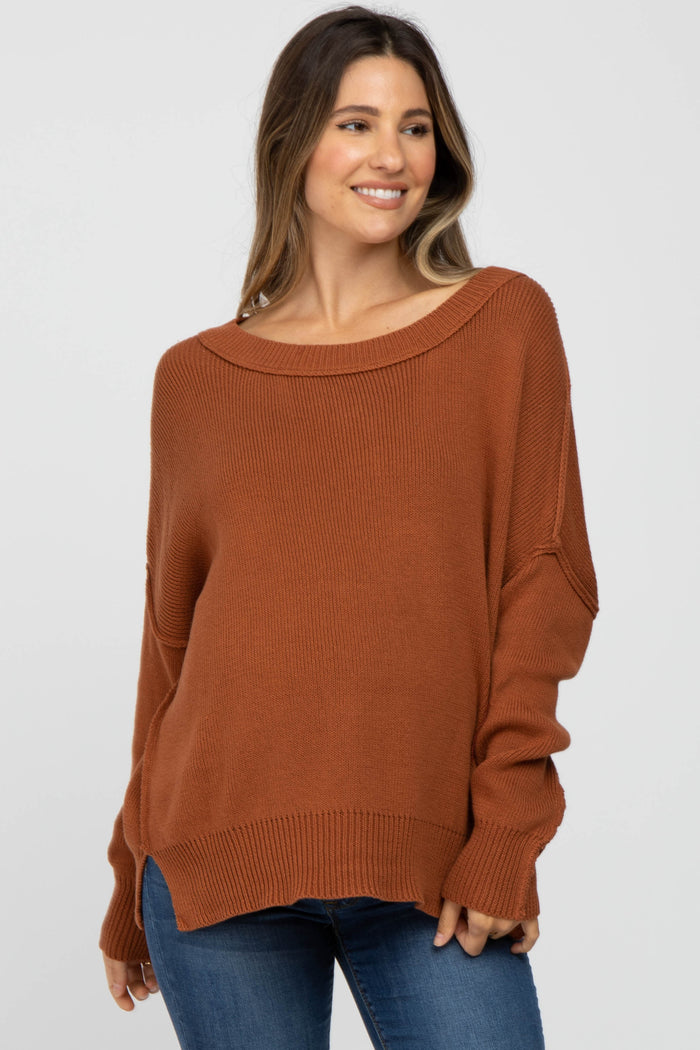 woman wearing a rust-colored oversized maternity sweater with a wide neckline and relaxed fit