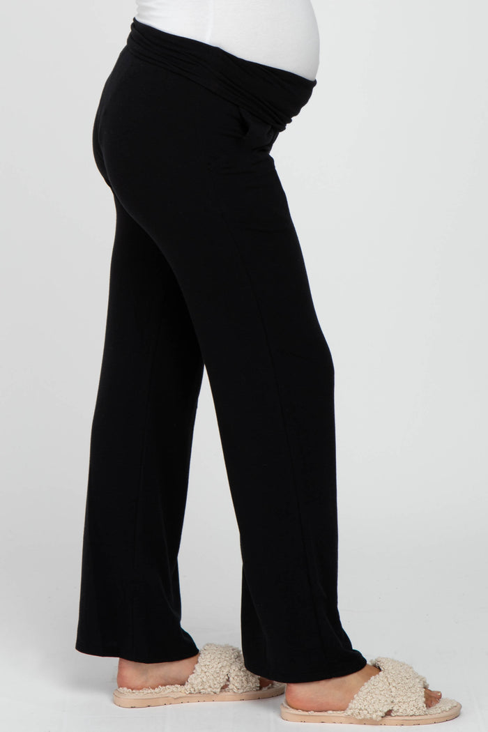 woman wearing black maternity pants with a wide waistband and a visible baby bump, paired with cozy slippers