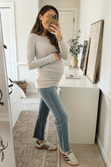 woman wearing a light gray long sleeve maternity top and jeans, holding her baby bump in front of a mirror