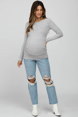 woman wearing a gray long sleeve maternity top and distressed light blue jeans with a visible baby bump