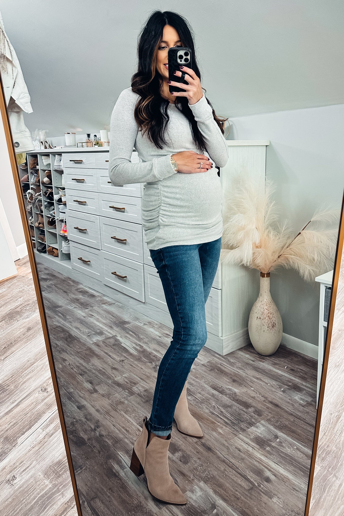 pregnant woman in grey long sleeve maternity top and blue jeans taking mirror selfie in a walk-in closet