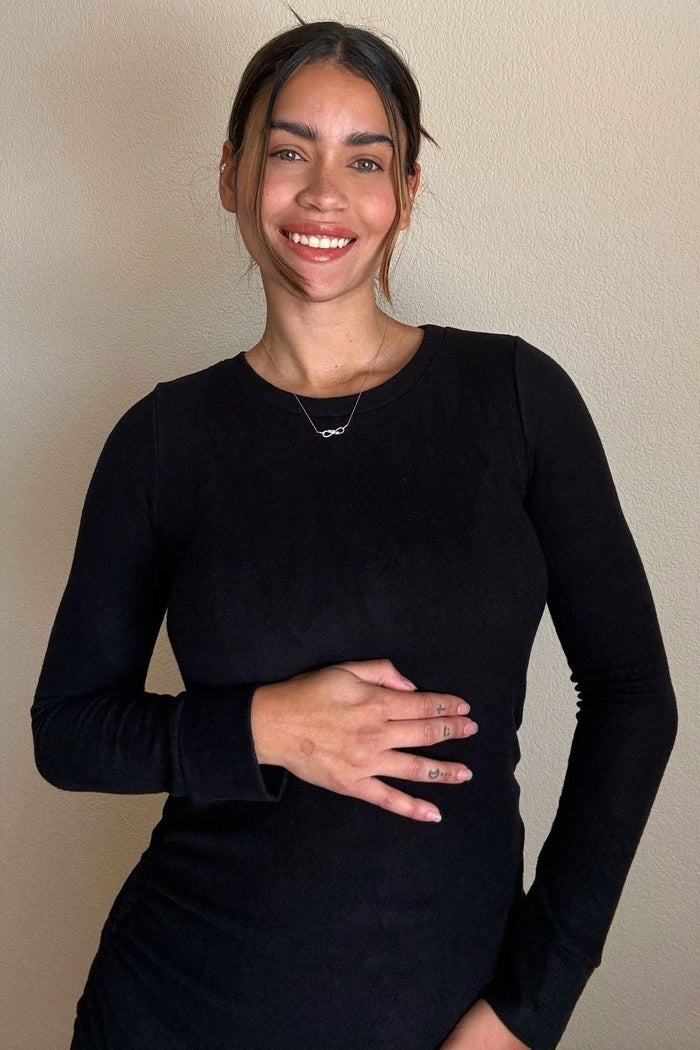 smiling woman in black long sleeve shirt with hand on stomach and infinity necklace