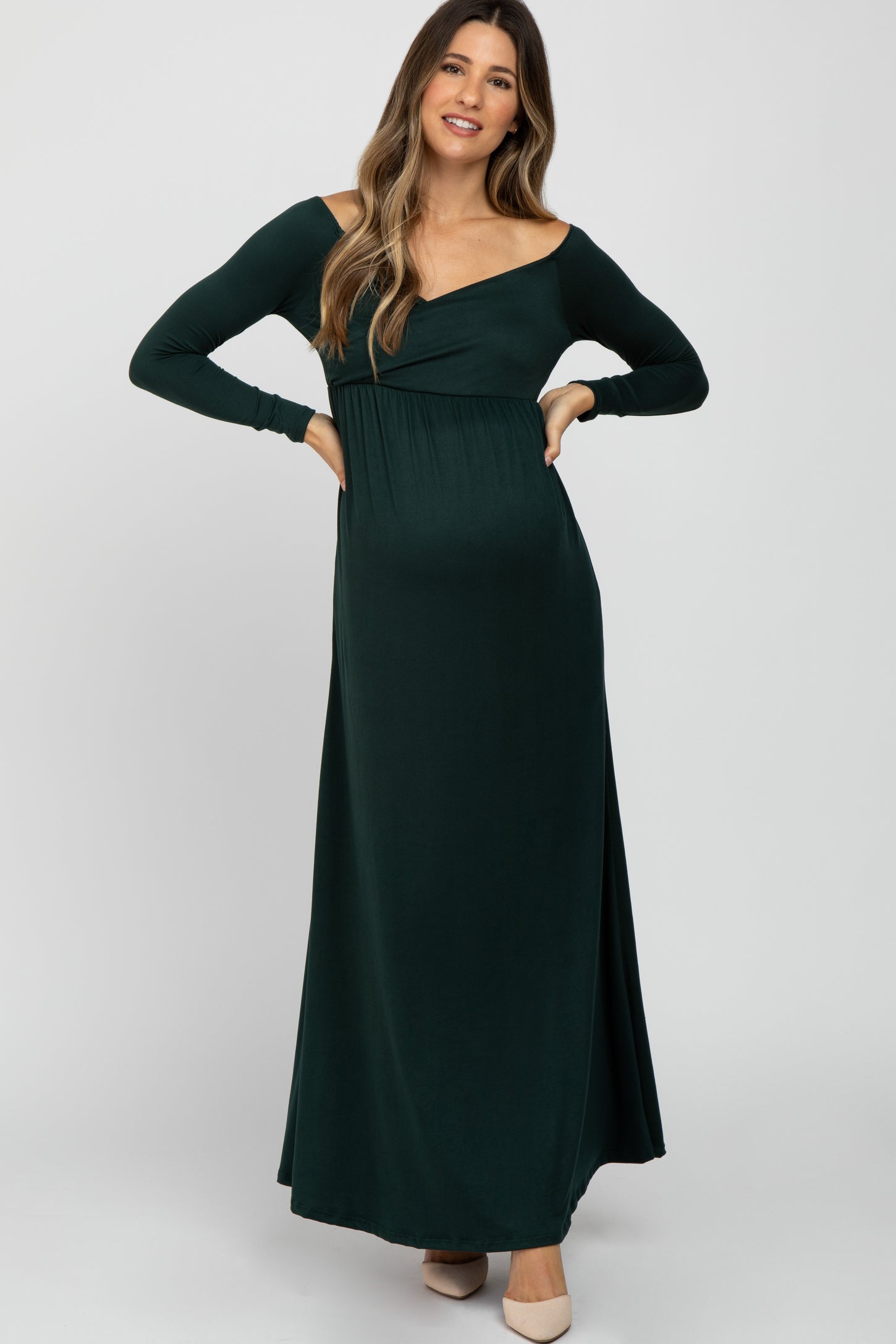 woman wearing a dark green off-shoulder maternity dress with long sleeves and a visible baby bump