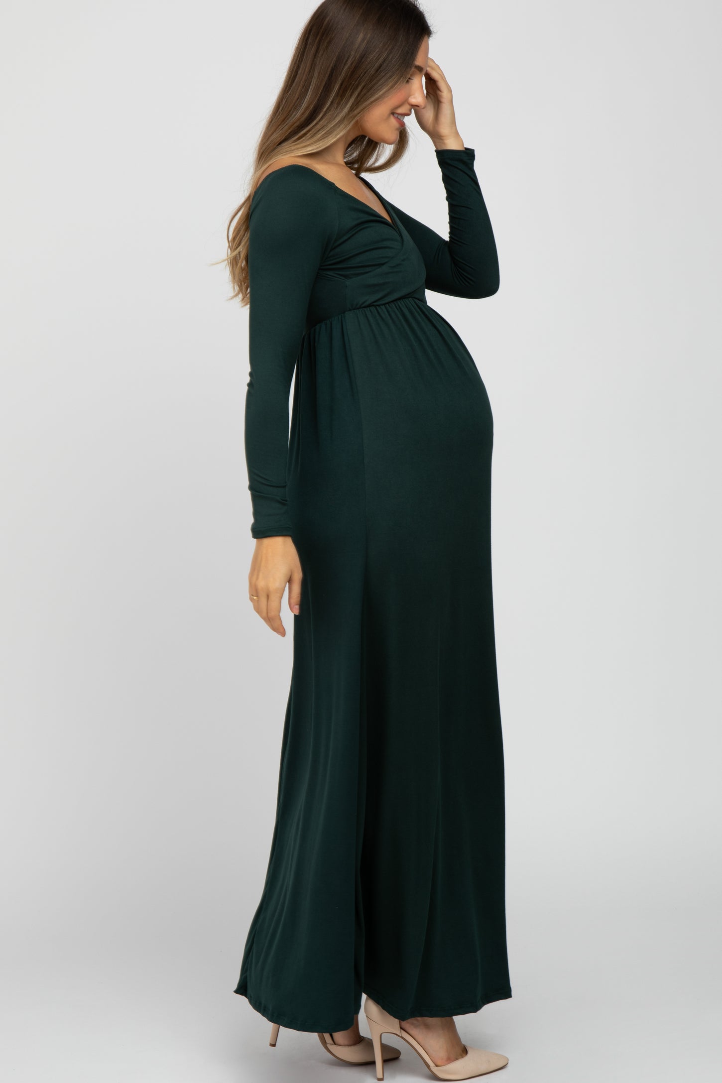 woman wearing a dark green long sleeve maternity dress with a fitted bodice and flowing skirt, showing her baby bump