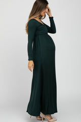 woman wearing a dark green long sleeve maternity dress with a fitted bodice and flowing skirt, showing her baby bump