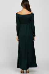 woman wearing a dark green off-shoulder maternity maxi dress with long sleeves, showing a flowing silhouette from the back