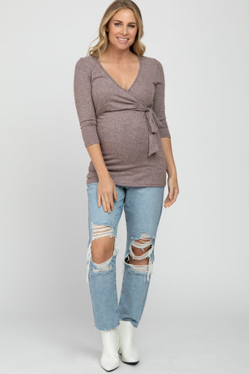 smiling pregnant woman wearing a mauve wrap maternity top and distressed blue jeans