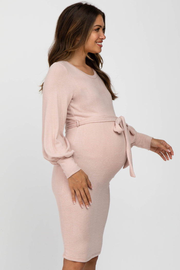 woman wearing a light pink long sleeve maternity dress with a tie detail at the waist and visible baby bump