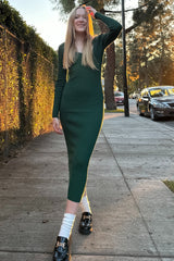 woman wearing a dark green ribbed midi dress with long sleeves and black loafers, walking on a sidewalk at sunset
