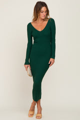 woman wearing a long green ribbed knit dress with a deep V-neck and long sleeves, holding a clutch purse