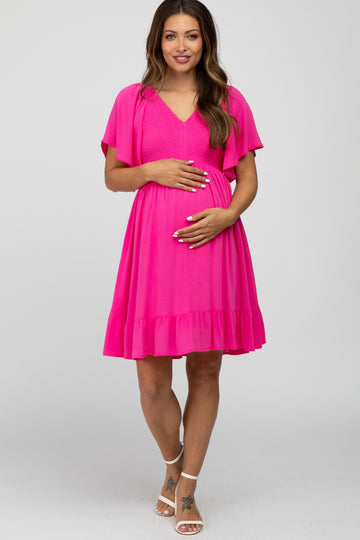 woman wearing a bright pink maternity dress with flutter sleeves and a ruffled hem, holding her baby bump