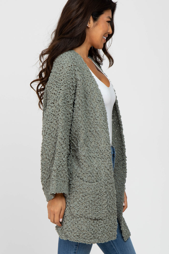 woman wearing a long sage green popcorn knit cardigan over a white top and blue jeans