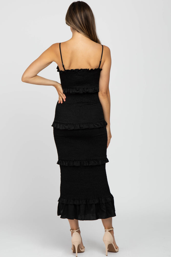 Back view of a woman wearing a black smocked tiered midi dress with spaghetti straps and beige heels