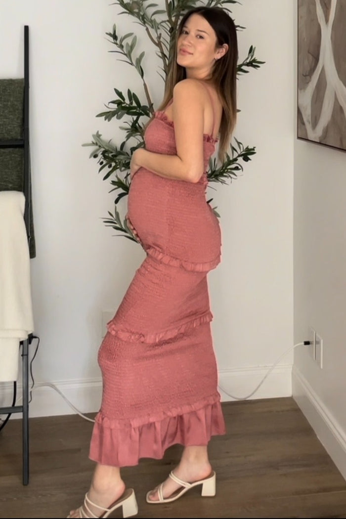 woman wearing a dusty rose strapless maternity dress with ruffle details, showing her baby bump while standing sideways
