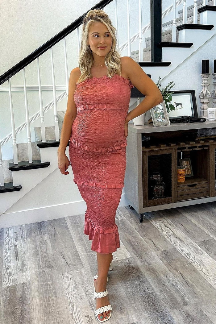 woman wearing a coral maternity dress with ruffles and a fitted silhouette, displaying her baby bump while standing by stairs