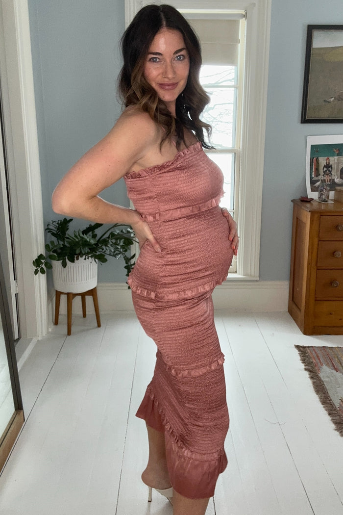 woman wearing a rust-colored maternity dress with ruffle details and a visible baby bump