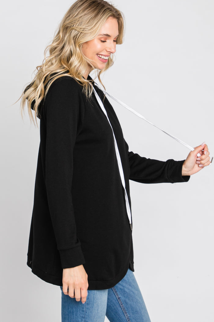 woman wearing a black zip-up hoodie with a white drawstring and long sleeves, styled with blue jeans