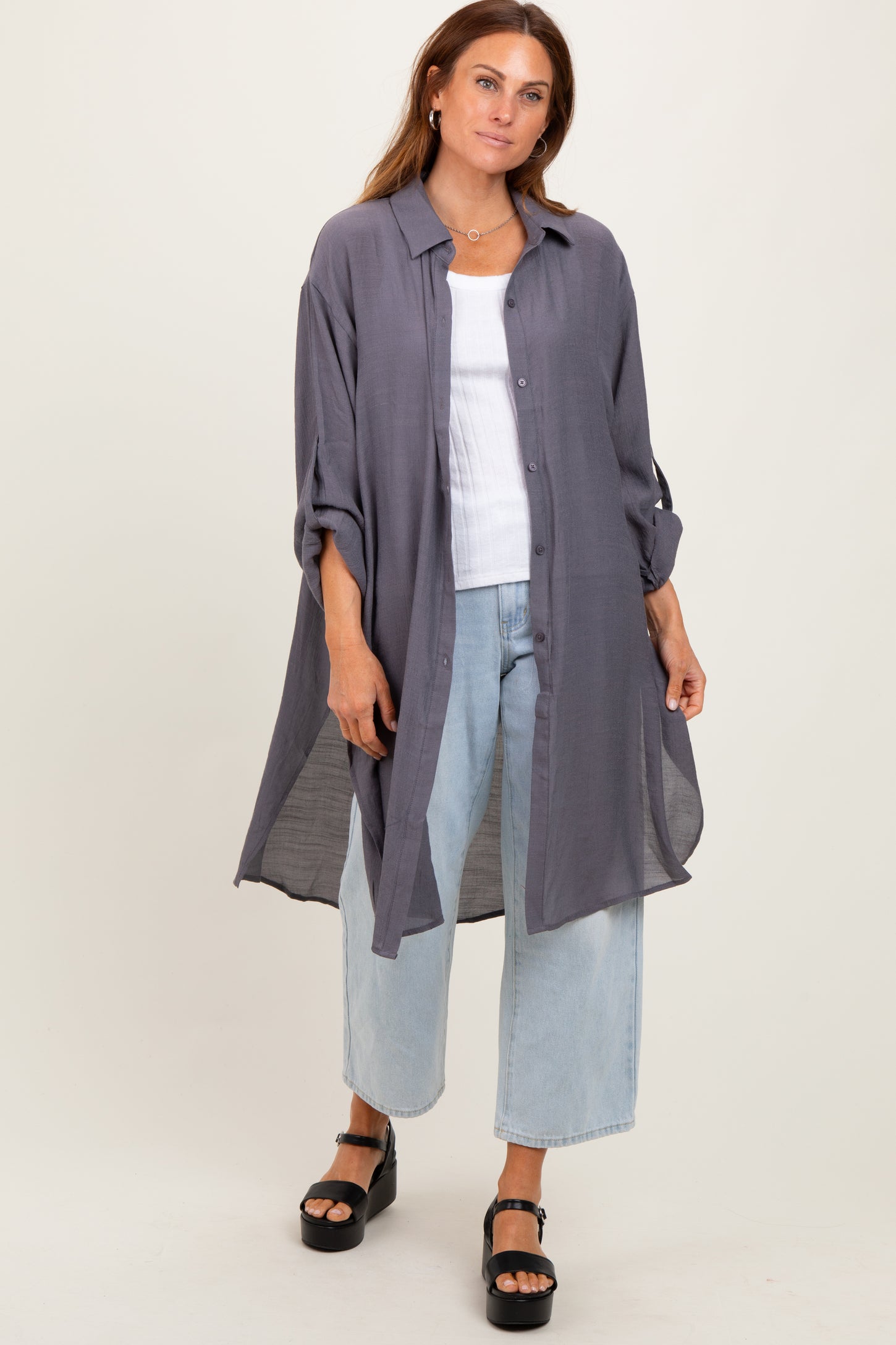 woman wearing a long grey button-up shirt, white tank top underneath, light blue wide-leg jeans, and black platform sandals