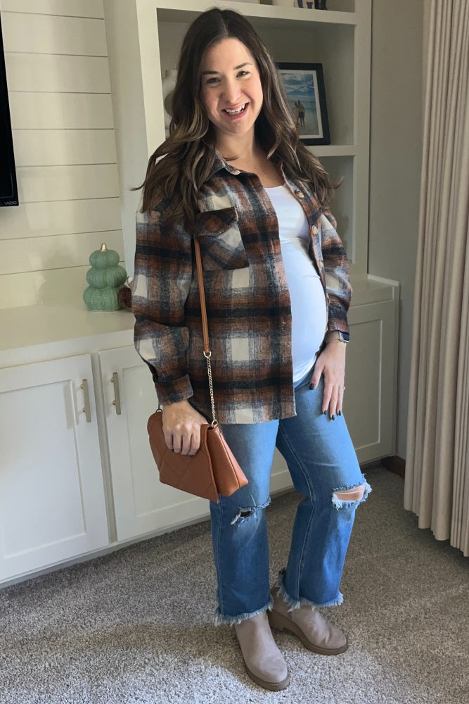 Smiling pregnant woman wearing a brown plaid shacket, white top, ripped jeans, and tan ankle boots.