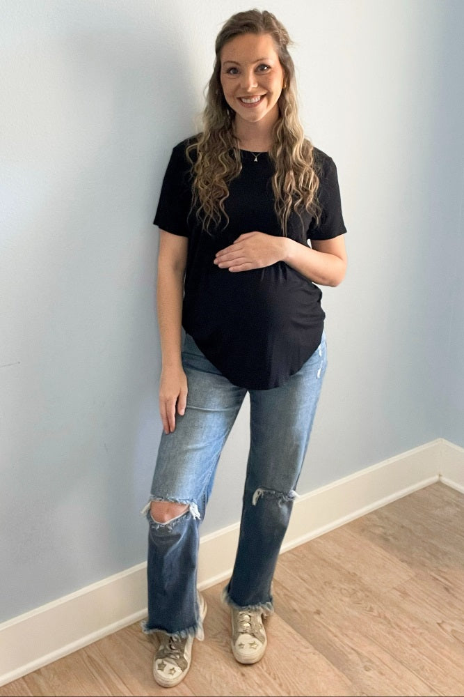 woman wearing a black short sleeve maternity top and distressed light blue jeans, holding her baby bump