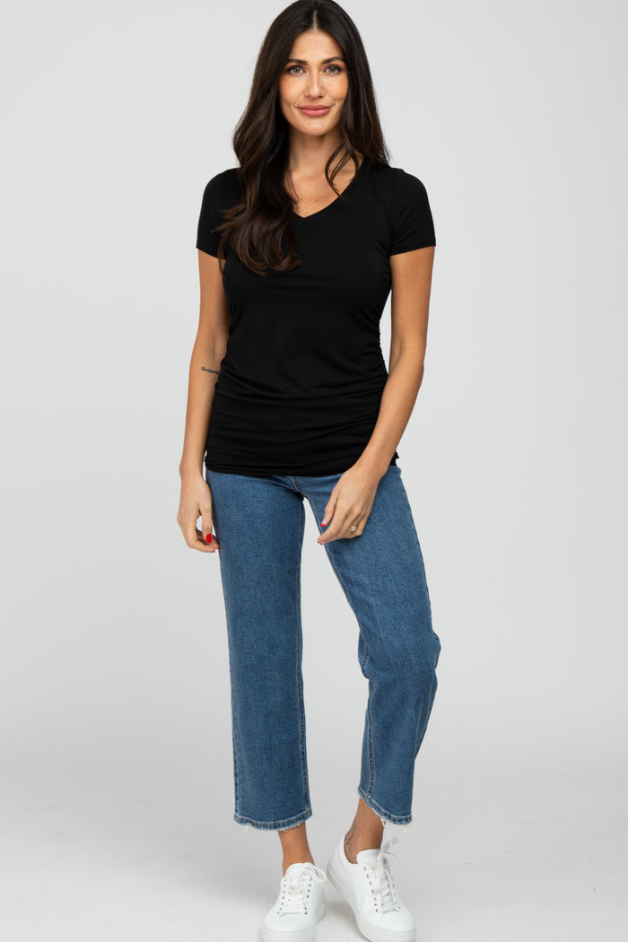 woman wearing a black short sleeve top with ruching and blue cropped jeans, standing and smiling