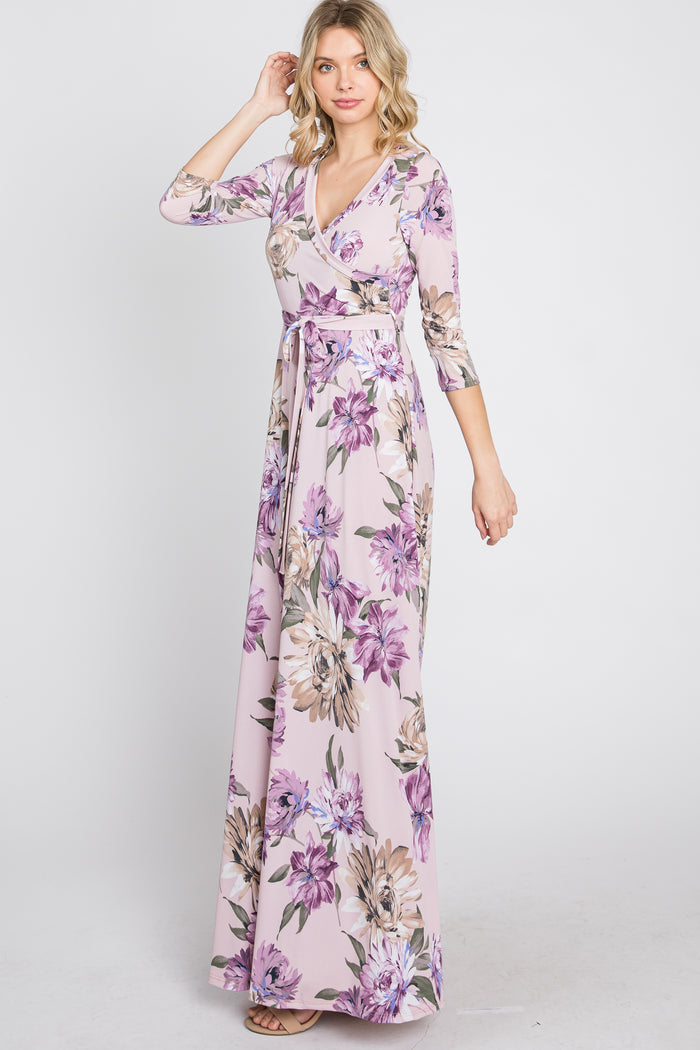 woman wearing a light pink floral print wrap maxi dress with three-quarter sleeves and a waist tie
