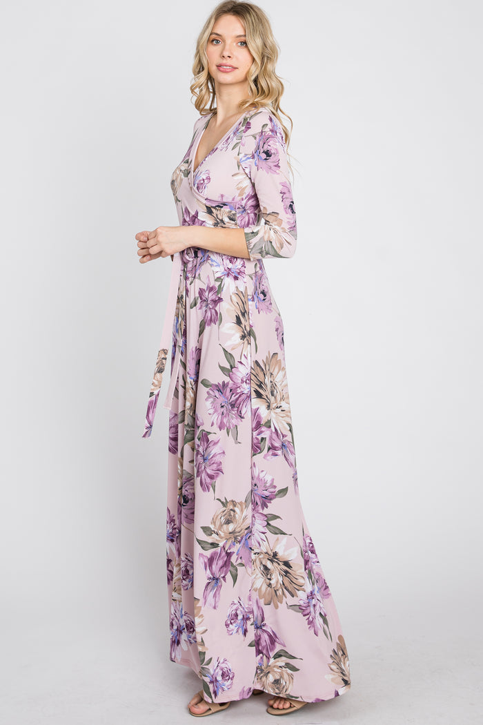 woman wearing a long sleeve floral maxi wrap dress in light pink with purple and tan flowers