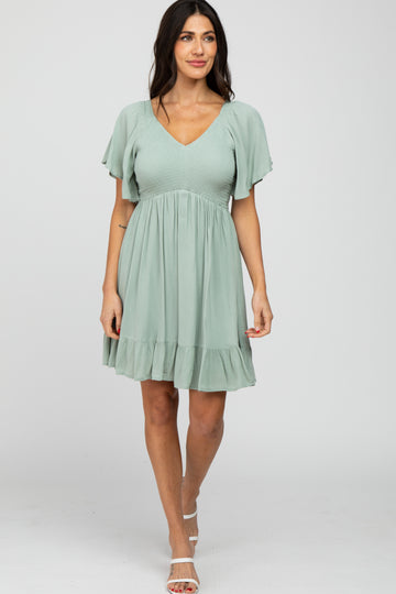 woman wearing a sage green v-neck maternity dress with flutter sleeves and a smocked bodice