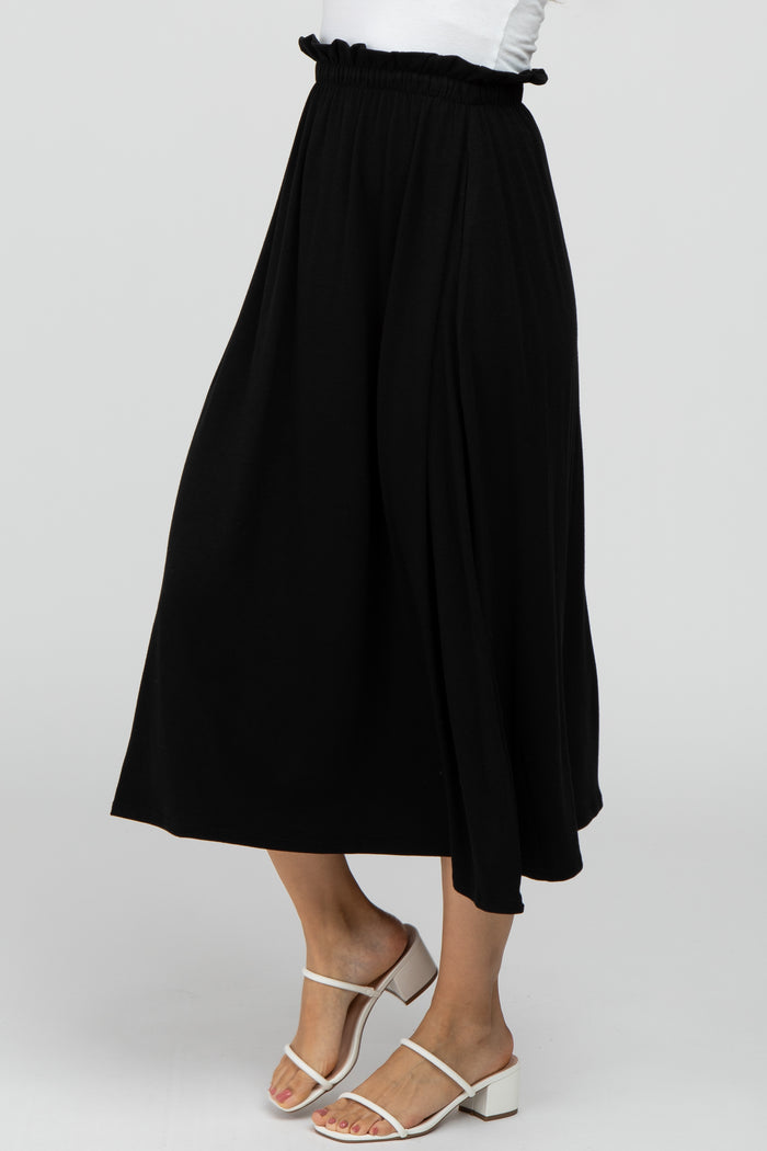 Woman wearing a black flowy midi skirt with a ruffled elastic waistband and white strappy heeled sandals