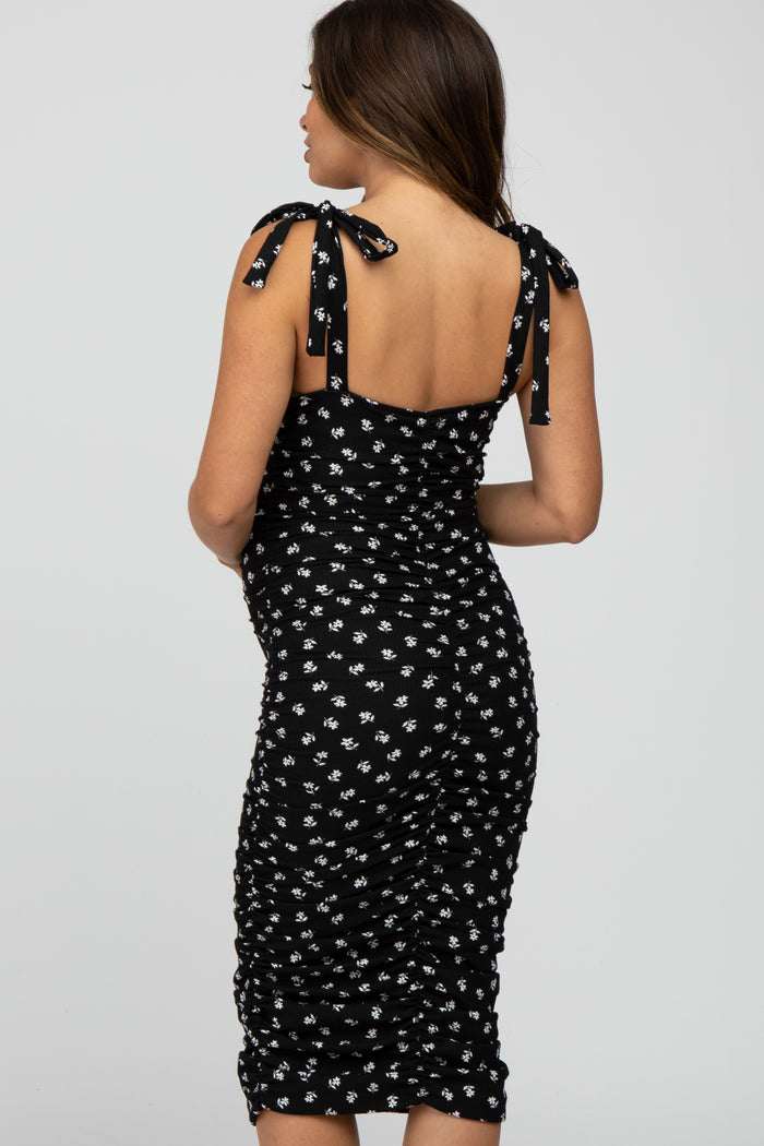 pregnant woman wearing a black floral ruched maternity dress with tie straps seen from the back