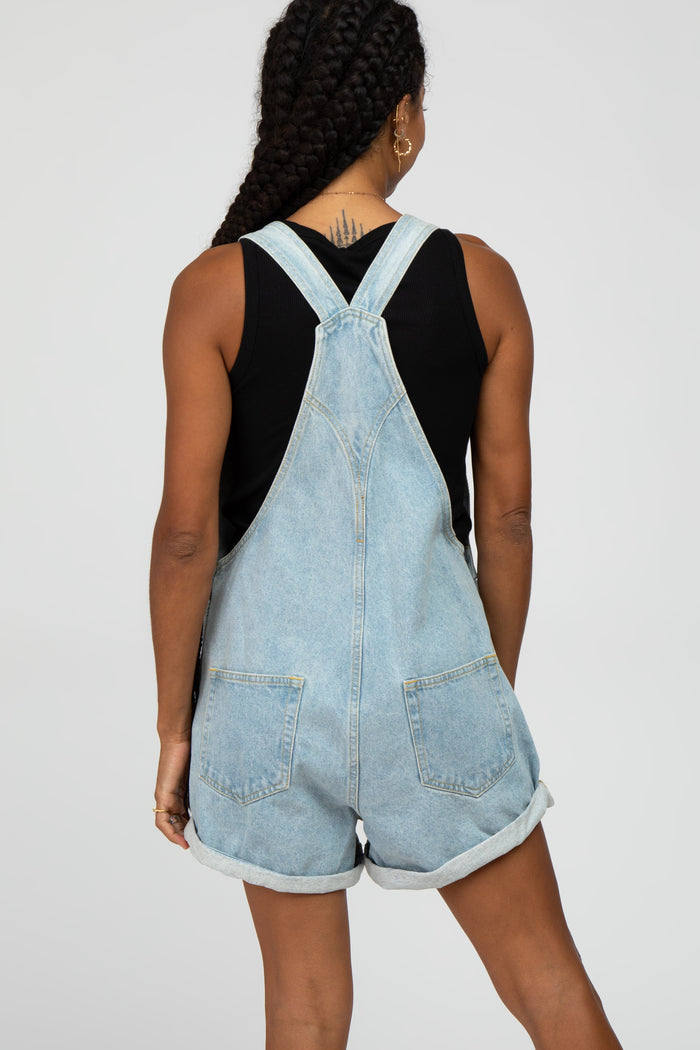woman wearing a light wash denim overall shorts with rolled hems and a black sleeveless top, seen from the back