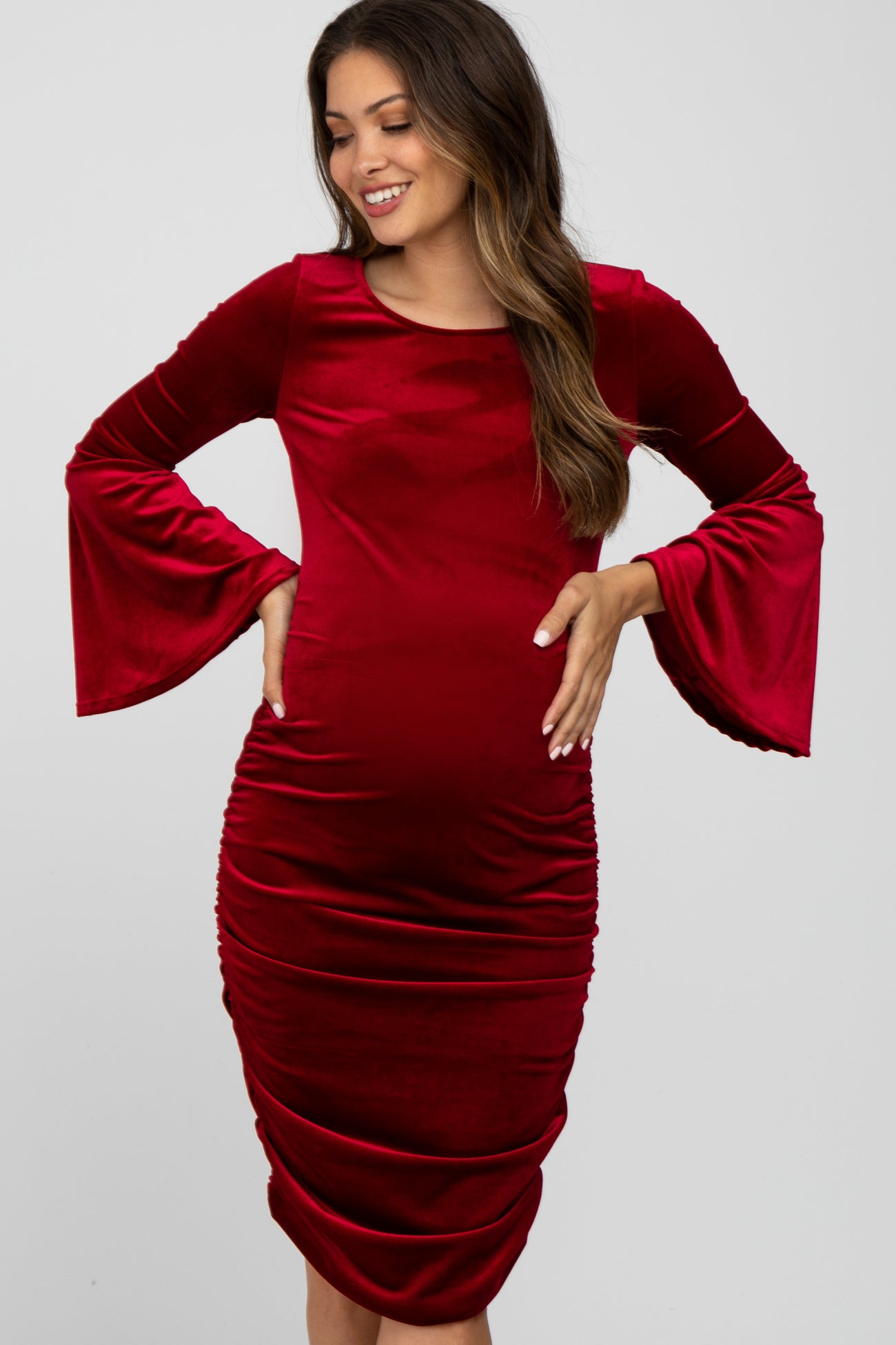 woman wearing a red velvet maternity dress with bell sleeves and gathered side detailing, highlighting her baby bump