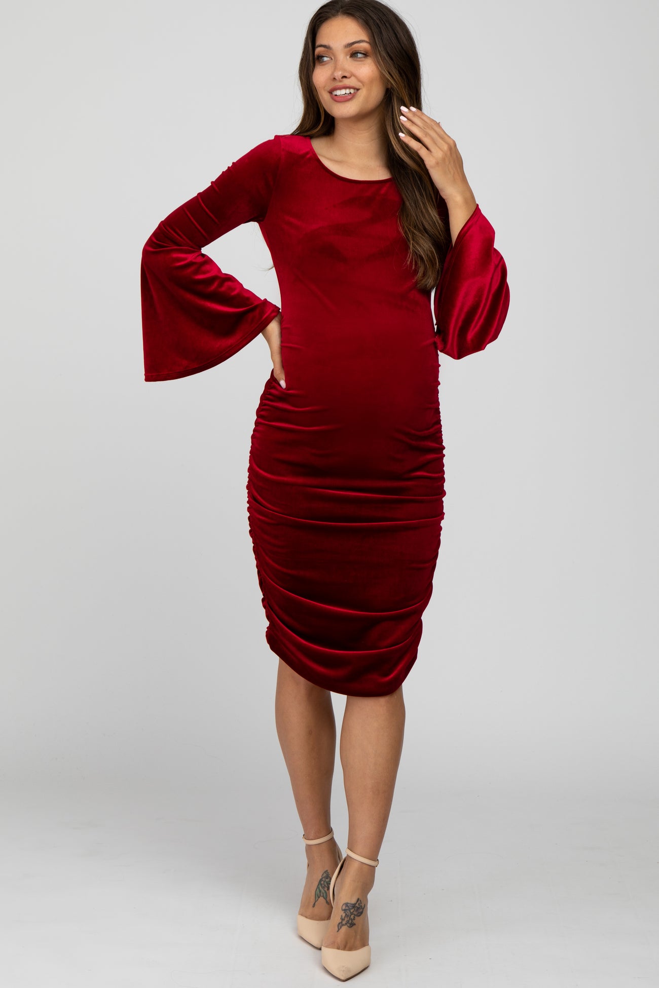 woman wearing a red velvet maternity dress with bell sleeves and side ruching, showing her baby bump