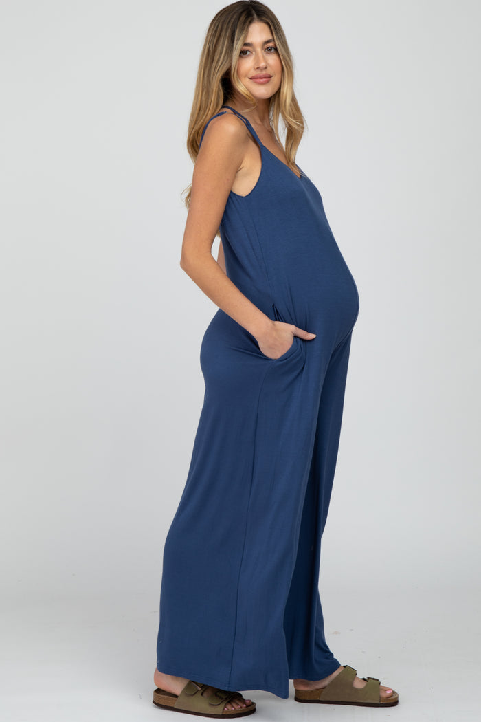 Pregnant woman wearing a blue wide-leg maternity jumpsuit with pockets and spaghetti straps
