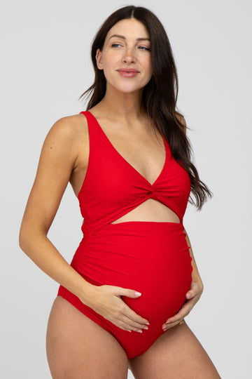 woman wearing a red maternity swimsuit with a twist front detail and showing her baby bump