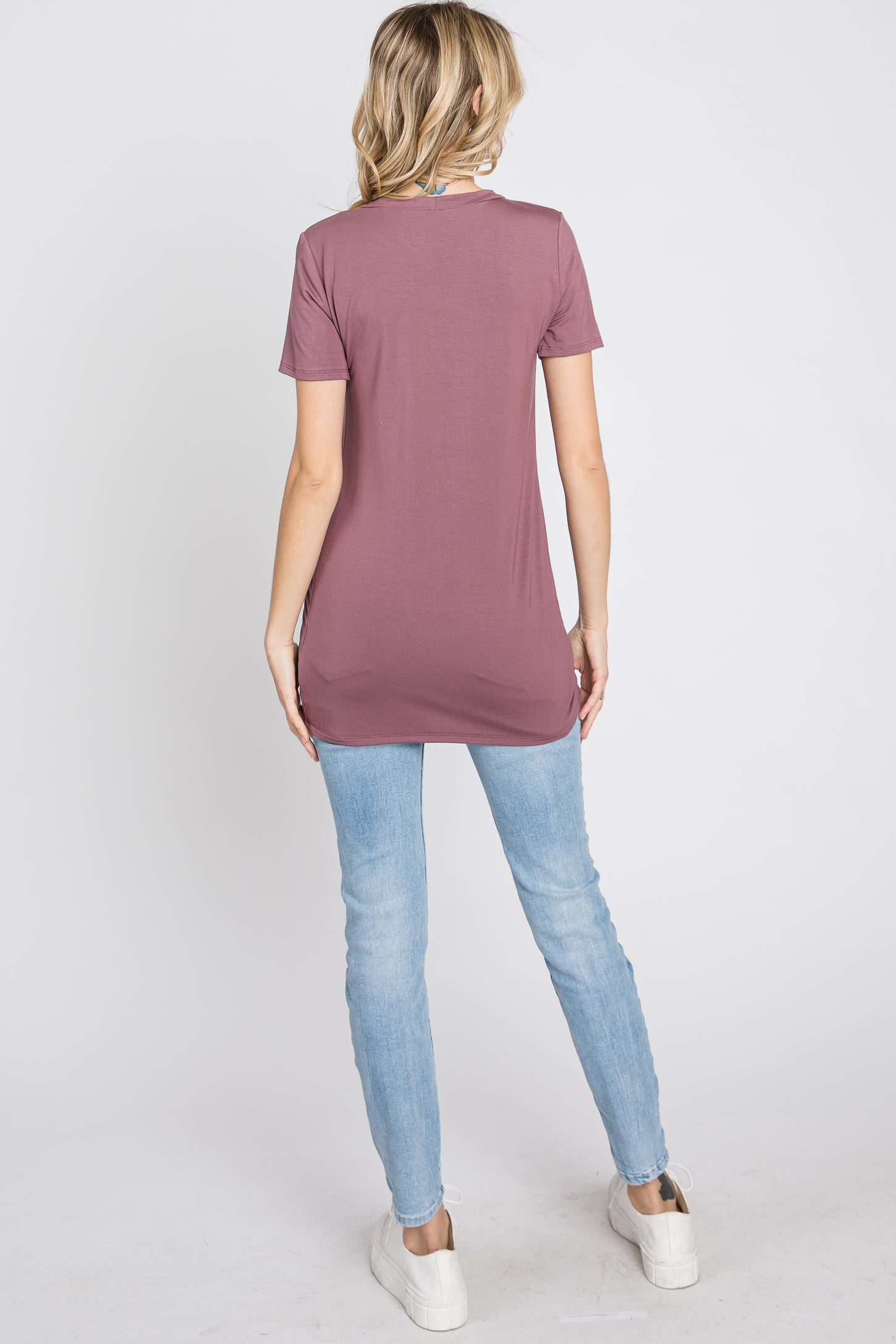 woman wearing a long mauve t-shirt with a relaxed fit and distressed light blue skinny jeans, viewed from the back