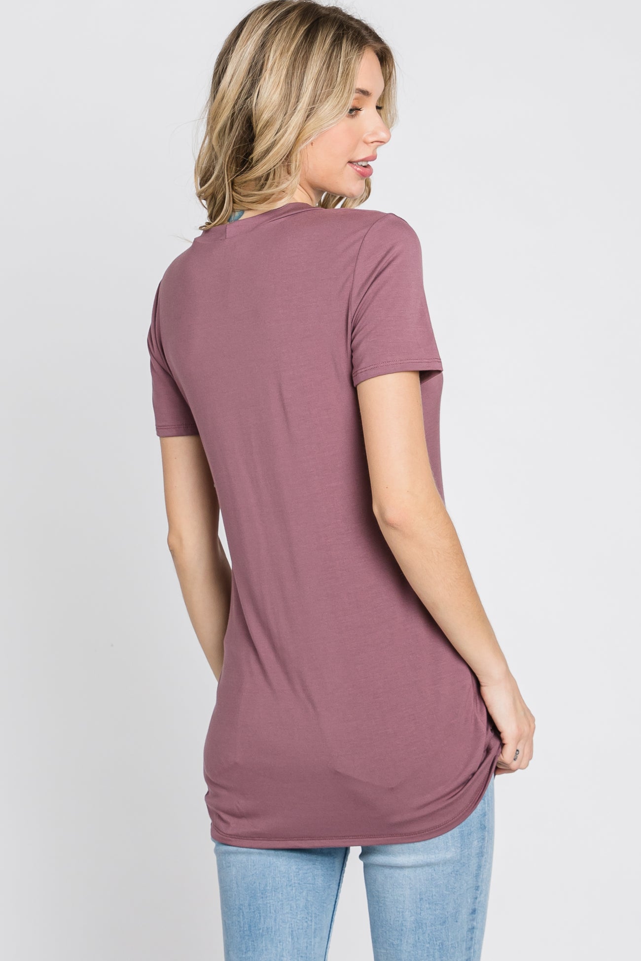 woman wearing a mauve short sleeve tunic top and light blue jeans, showing the back view of the top